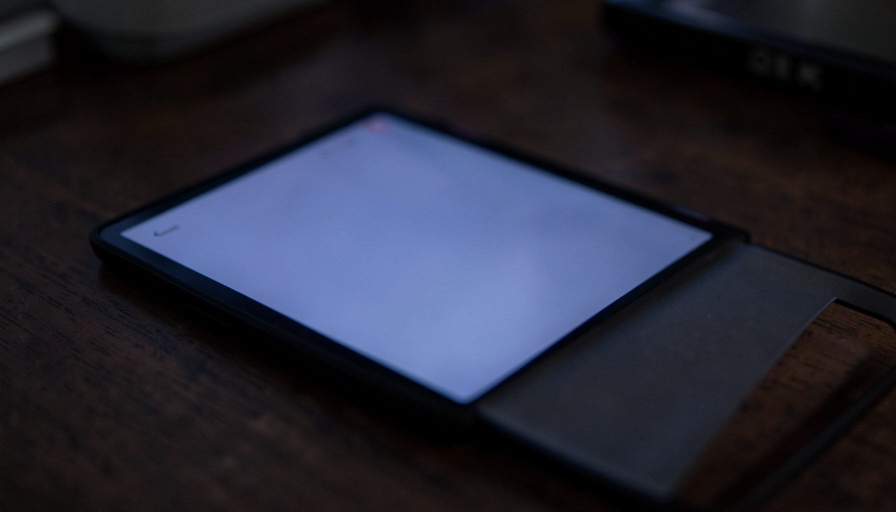 A close-up of an open ebook reader screen glowing softly in navy and lavender-grey tones against a dark wooden desk, quiet and studious mood
