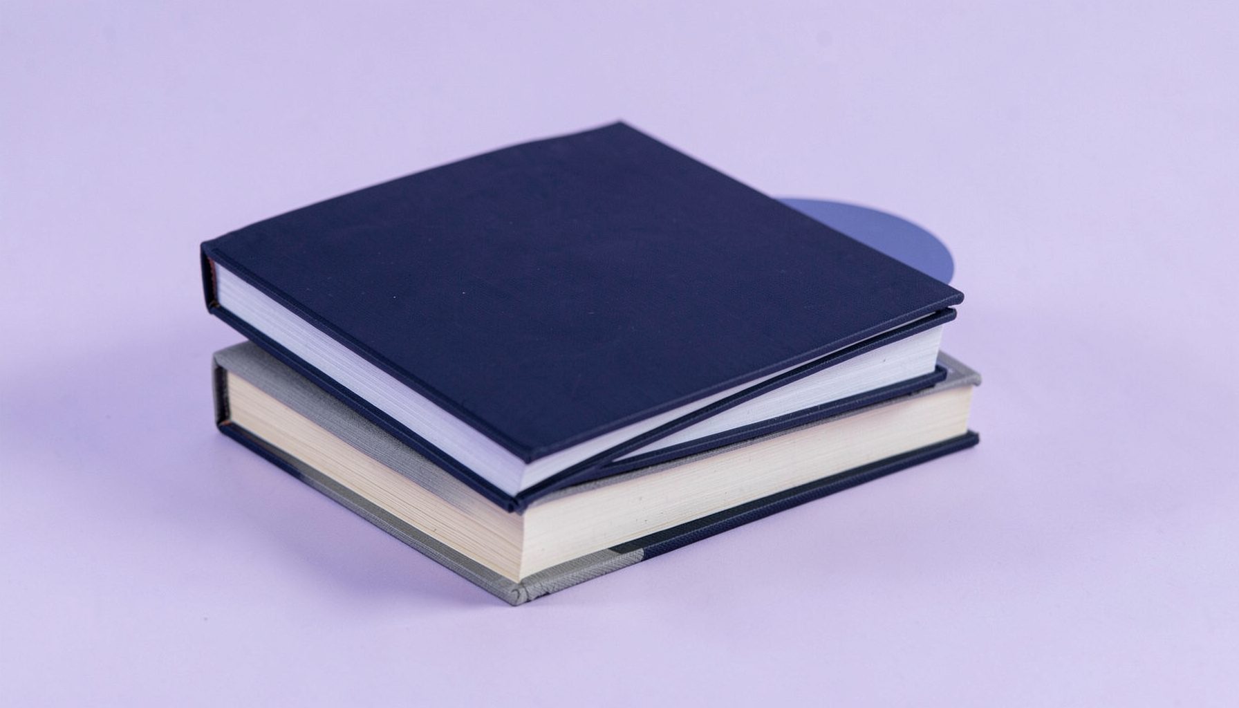 A stack of academic textbooks with plain navy and grey covers on a light lavender background, tidy and professional mood